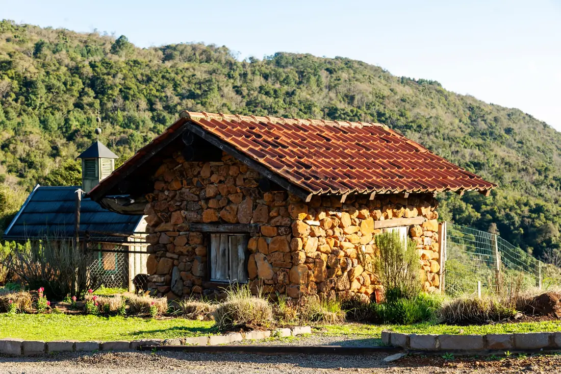 El Tejado: casa de piedra con techo de teja roja entre árboles y lomas